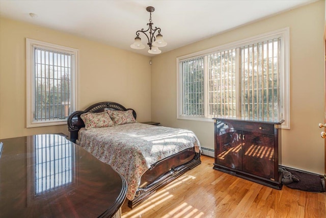 bedroom featuring an inviting chandelier, a baseboard heating unit, and wood finished floors