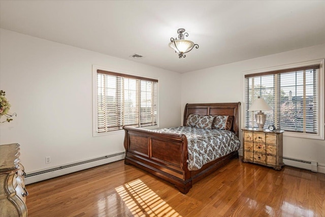 bedroom featuring a baseboard heating unit, wood finished floors, and visible vents