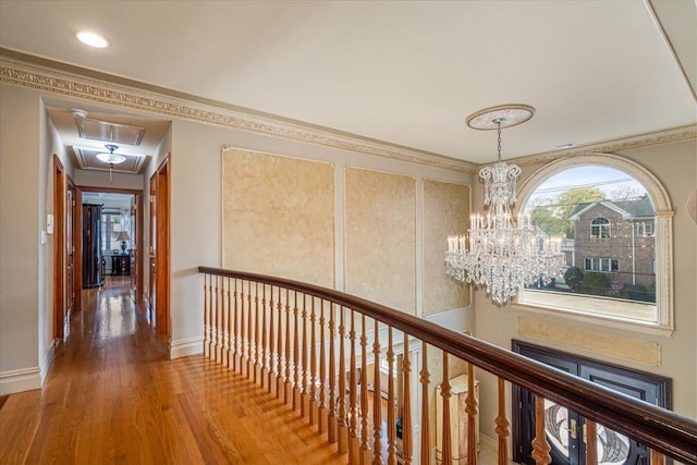 hallway with ornamental molding, wood finished floors, baseboards, a chandelier, and an upstairs landing