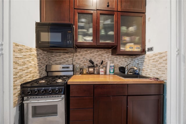 kitchen featuring glass insert cabinets, a sink, black microwave, stainless steel gas range, and butcher block countertops