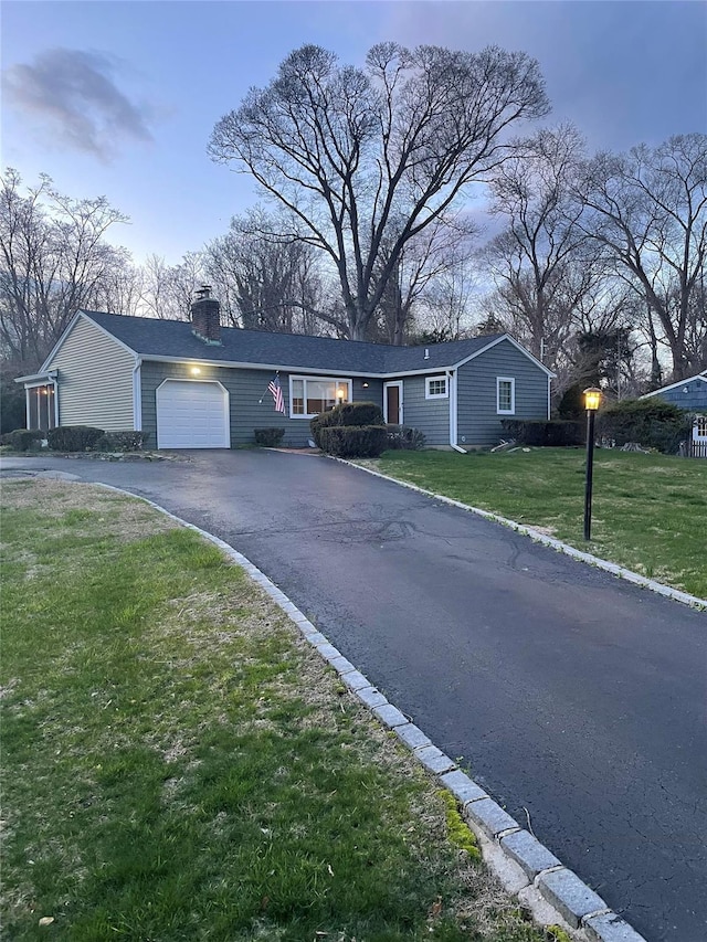 single story home with a front lawn, an attached garage, a chimney, and driveway