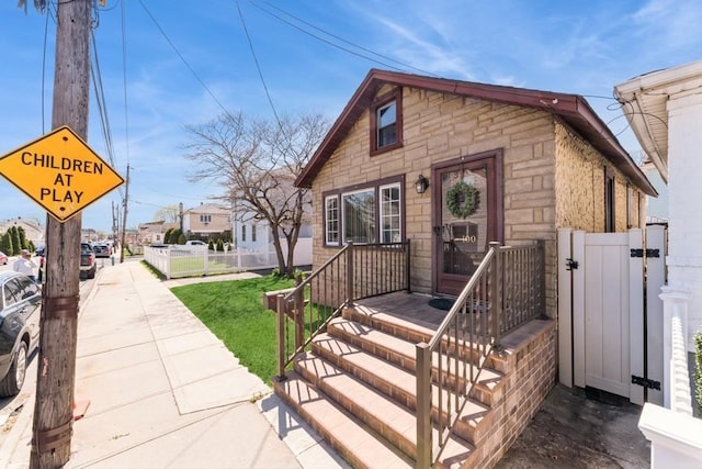 view of front of home with stone siding, fence, a front yard, and a gate