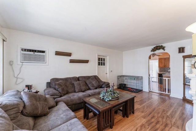 living area featuring light wood finished floors, visible vents, arched walkways, and a wall mounted air conditioner