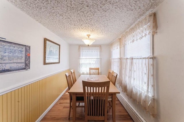dining space featuring wainscoting, wood finished floors, and a textured ceiling