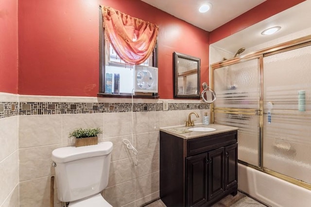 full bath featuring a wainscoted wall, toilet, tile walls, combined bath / shower with glass door, and vanity