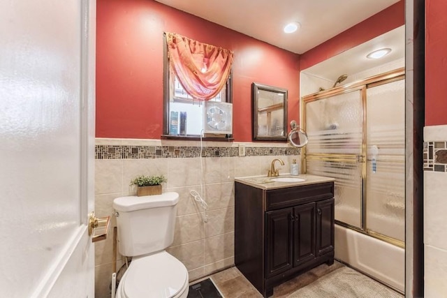 bathroom with shower / bath combination with glass door, a wainscoted wall, toilet, vanity, and tile walls