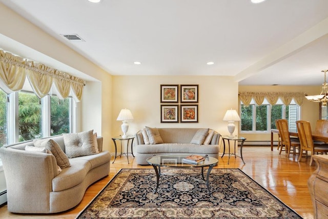 living room featuring a wealth of natural light, light wood-style flooring, visible vents, and an inviting chandelier