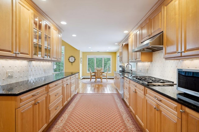 kitchen featuring light wood finished floors, under cabinet range hood, dark stone countertops, dishwasher, and gas stovetop