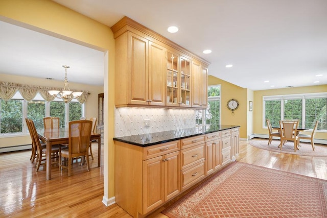kitchen with glass insert cabinets, an inviting chandelier, decorative backsplash, and light wood-type flooring