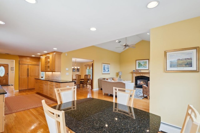 dining area featuring baseboard heating, a glass covered fireplace, ceiling fan with notable chandelier, and light wood-type flooring