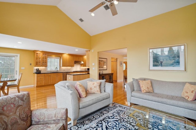 living area featuring high vaulted ceiling, a ceiling fan, visible vents, and light wood finished floors
