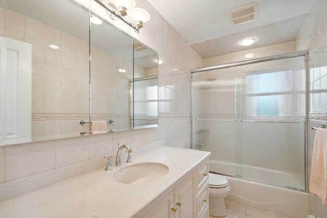 bathroom featuring vanity, tile walls, visible vents, toilet, and shower / bath combination with glass door