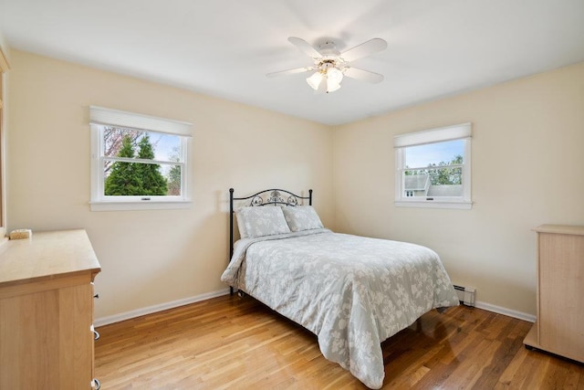 bedroom featuring a baseboard radiator, baseboards, ceiling fan, and light wood finished floors