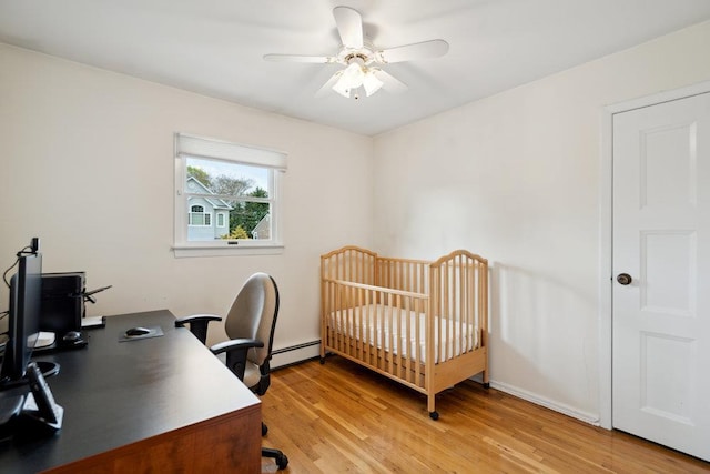 bedroom featuring a baseboard heating unit, a crib, light wood-type flooring, and ceiling fan