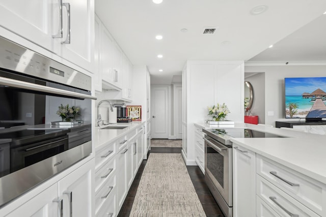 kitchen with a sink, appliances with stainless steel finishes, light countertops, white cabinetry, and visible vents