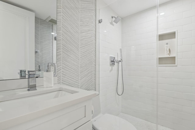 bathroom featuring a tile shower, toilet, and vanity