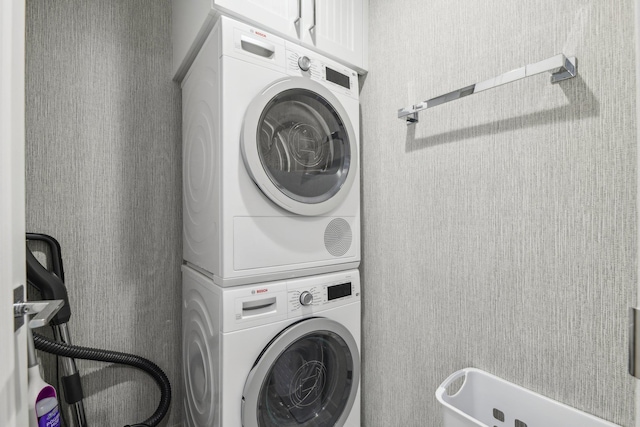 washroom featuring stacked washer / drying machine and cabinet space