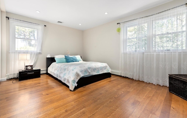bedroom featuring a baseboard heating unit, wood finished floors, visible vents, recessed lighting, and a baseboard radiator