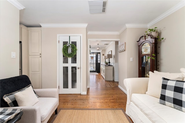 living room with light wood-type flooring, visible vents, crown molding, and baseboards
