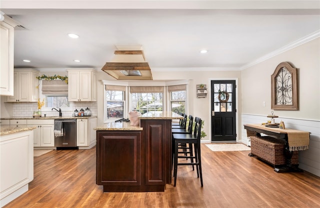 kitchen with stainless steel dishwasher, ornamental molding, a sink, light wood-type flooring, and a kitchen bar