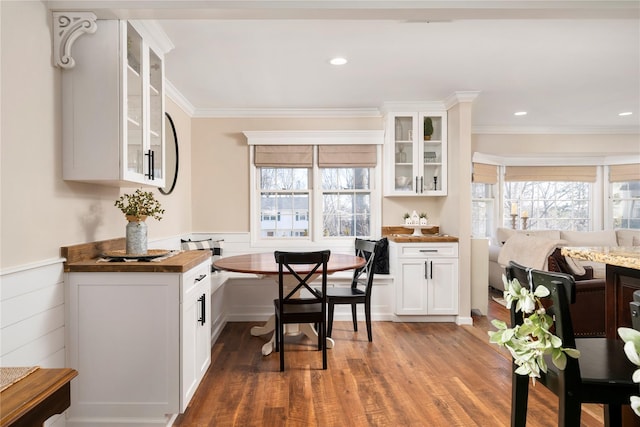 kitchen featuring wood finished floors, breakfast area, ornamental molding, and glass insert cabinets