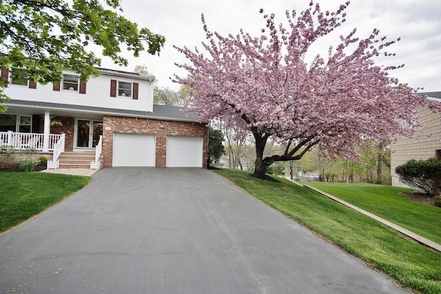view of front of property with a front lawn, driveway, covered porch, and brick siding