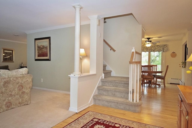 staircase with a baseboard radiator, ceiling fan, ornamental molding, decorative columns, and wood finished floors