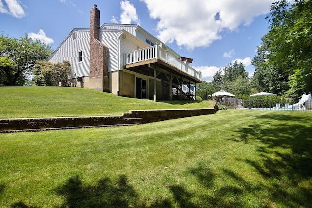 rear view of house with a wooden deck, a yard, fence, and a chimney