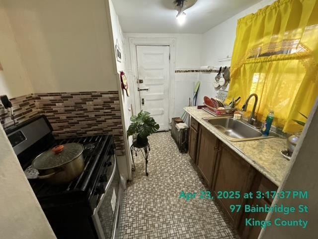 kitchen featuring electric range, tile walls, wainscoting, a sink, and light countertops
