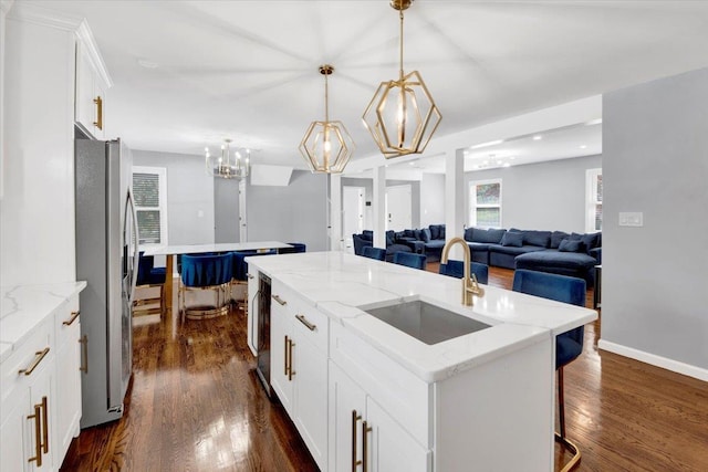 kitchen featuring open floor plan, an island with sink, stainless steel fridge, dark wood-type flooring, and a sink