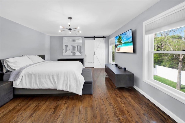 bedroom with wood finished floors, baseboards, a barn door, and a notable chandelier