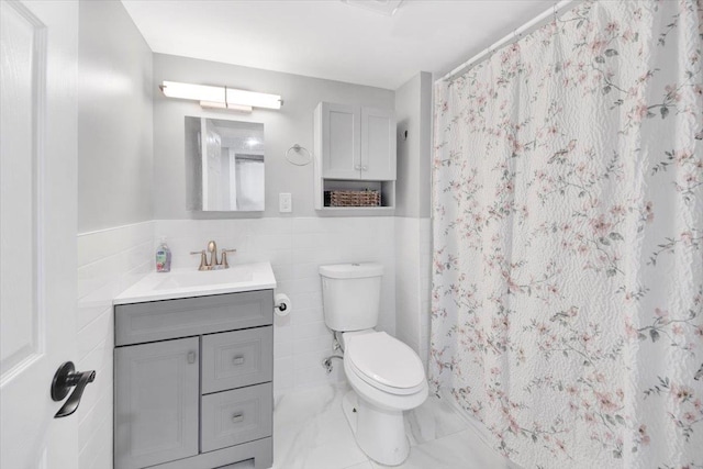 bathroom featuring tile walls, a wainscoted wall, vanity, toilet, and marble finish floor