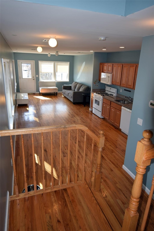 kitchen featuring brown cabinetry, light wood-style flooring, white appliances, and a sink