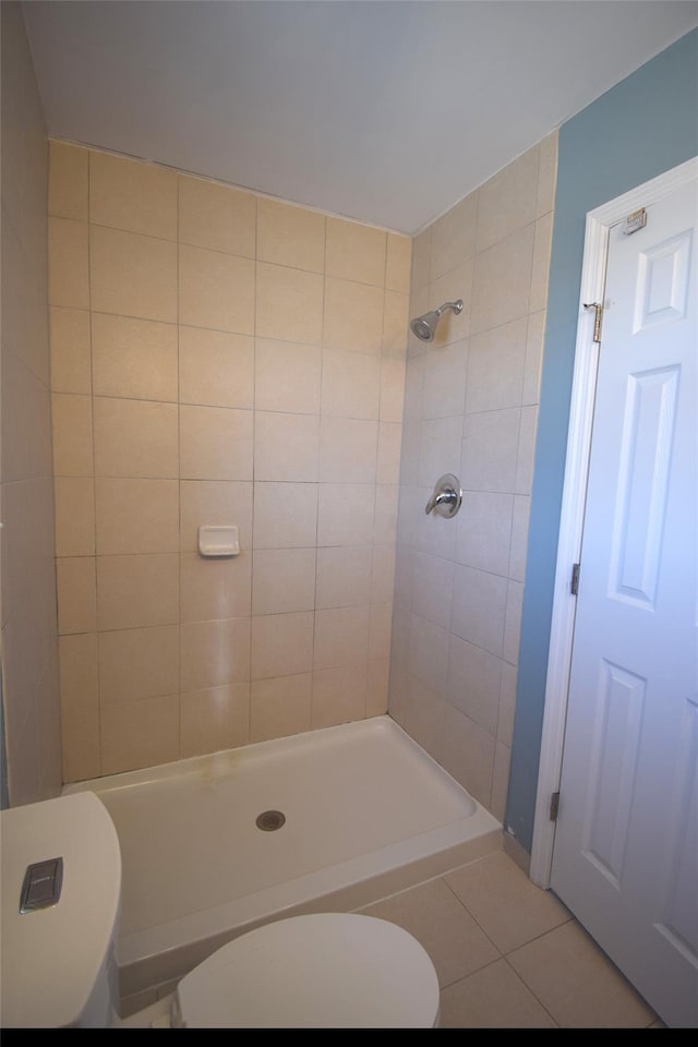 bathroom with toilet, tile patterned flooring, and a tile shower
