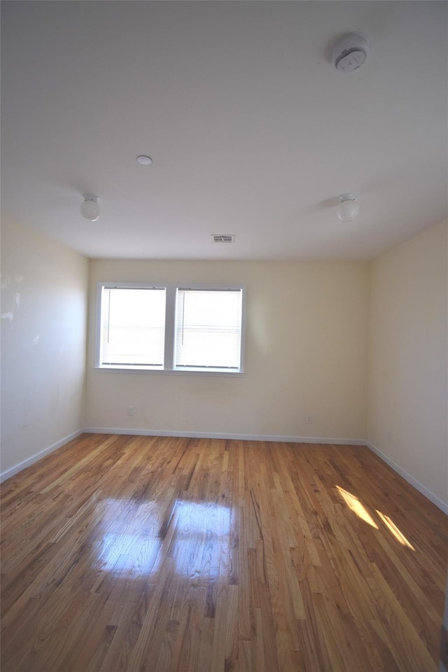unfurnished room featuring baseboards, wood finished floors, and visible vents