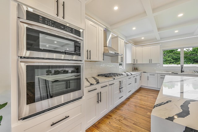 296 Division Ave, Hicksville, NY 11801 - kitchen with stainless steel appliances, wall chimney range hood, light wood-type flooring, coffered ceiling, and white cabinetry