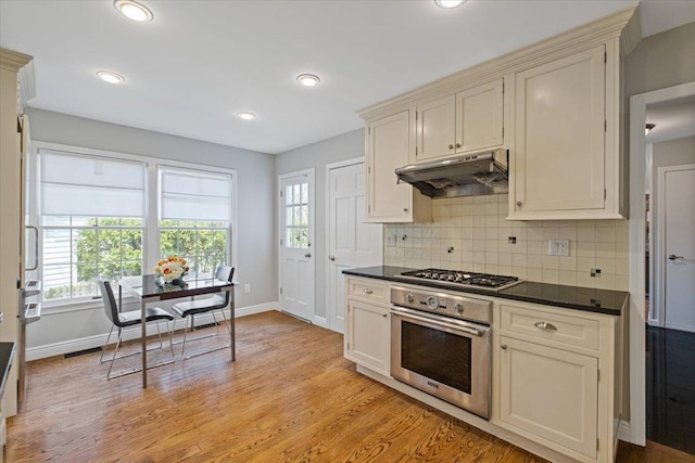 kitchen featuring decorative backsplash, dark countertops, baseboards, under cabinet range hood, and stainless steel appliances