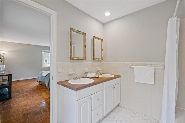 ensuite bathroom with double vanity, tile walls, a sink, and a wainscoted wall