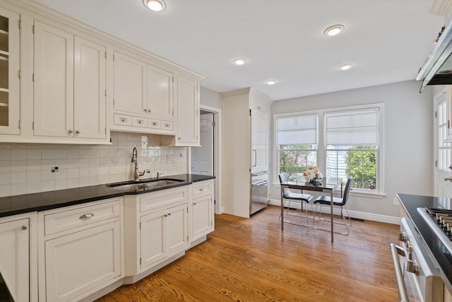 kitchen with dark countertops, tasteful backsplash, a sink, baseboards, and light wood-style floors