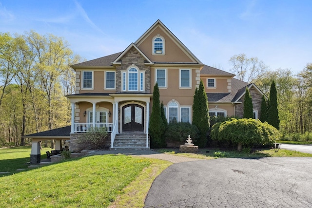 view of front of home featuring a front lawn, stone siding, stucco siding, a porch, and french doors
