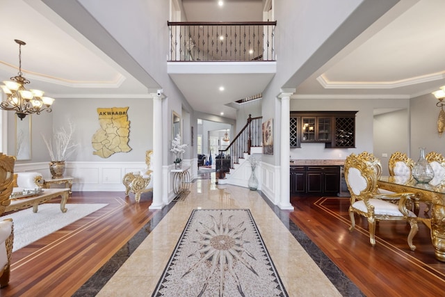 entrance foyer with crown molding, stairs, decorative columns, a decorative wall, and a high ceiling