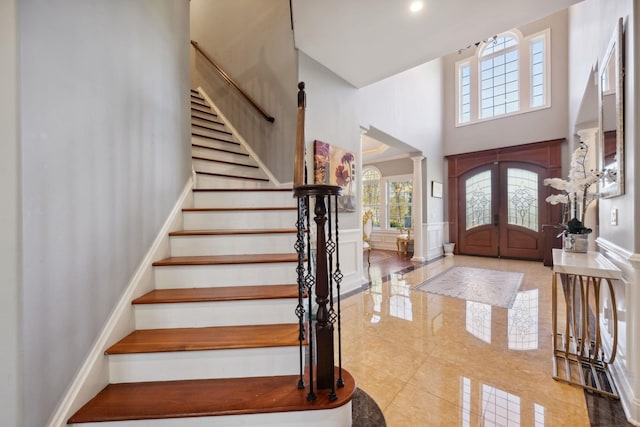 foyer with stairs, a wainscoted wall, a high ceiling, a decorative wall, and ornate columns