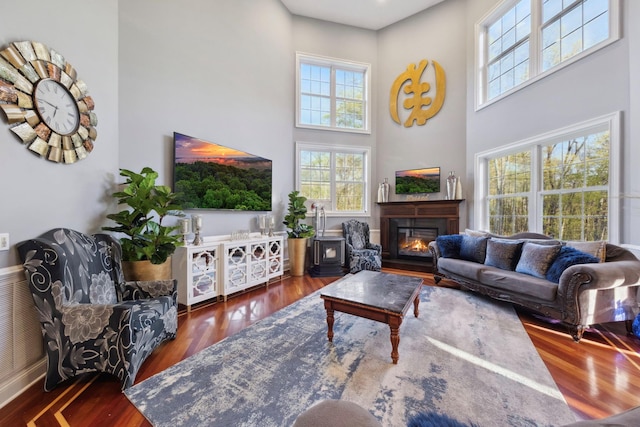 living room featuring a glass covered fireplace, plenty of natural light, wood finished floors, and a towering ceiling