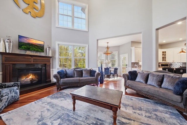 living area with a glass covered fireplace, a chandelier, wood finished floors, and a towering ceiling
