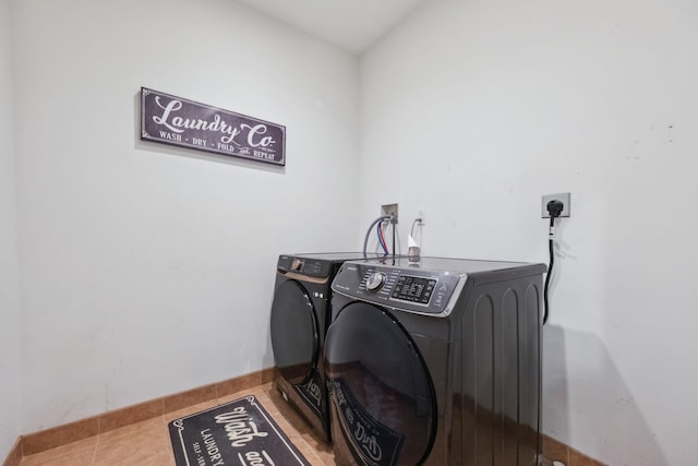 clothes washing area featuring laundry area, baseboards, tile patterned flooring, and washing machine and clothes dryer
