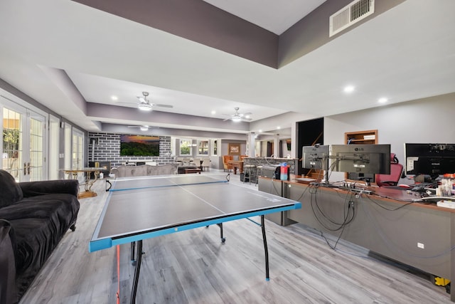 rec room with ceiling fan, visible vents, wood finished floors, a tray ceiling, and a wealth of natural light
