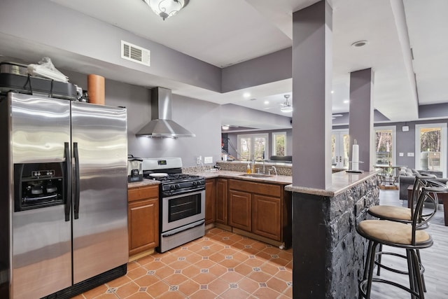 kitchen with a breakfast bar area, visible vents, appliances with stainless steel finishes, a sink, and wall chimney exhaust hood