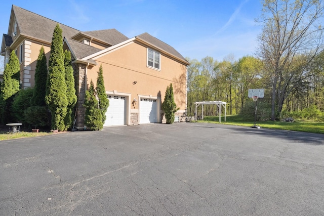 view of home's exterior with aphalt driveway, stone siding, roof with shingles, stucco siding, and an attached garage