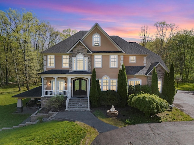 view of front of house with a front lawn, stone siding, stucco siding, french doors, and covered porch