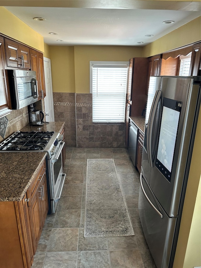 kitchen with dark stone counters, stone finish floor, stainless steel appliances, and tile walls
